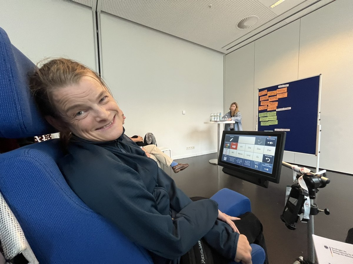 Nele Diercks am Sprachcomputer beim World-Caf&eacute;; im Hintergrund eine Metaplan-Wand mit den Themen Partizipation, Herausforderungen und Zukunftsperspektiven