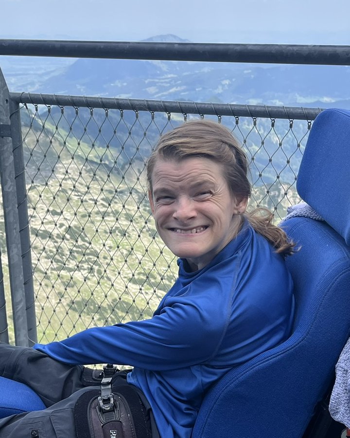 Nele Diercks l&auml;chelt im Rollstuhl auf einer Aussichtsplattform in den Bergen, neben ihr der Sprachcomputer