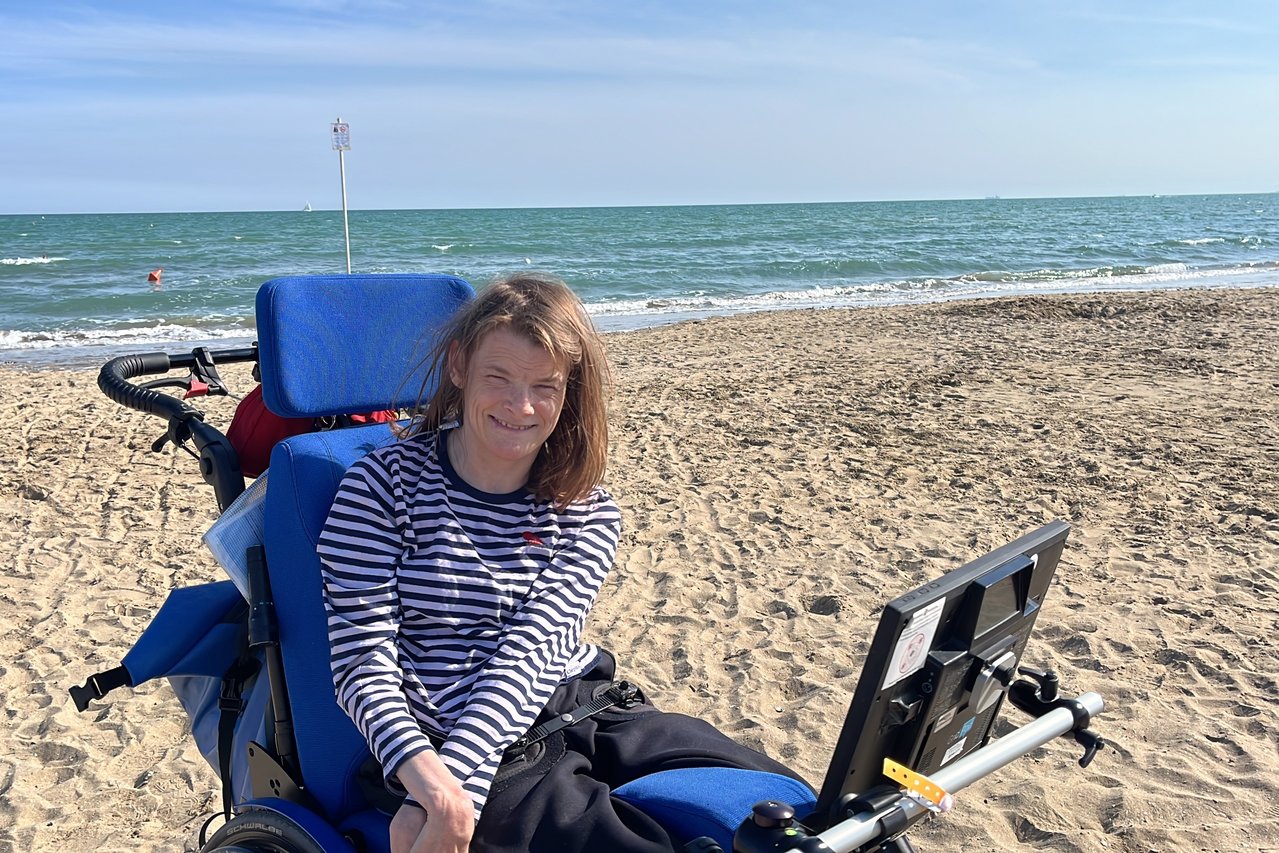 Nele Diercks im Rollstuhl am Strand, im Hintergrund das Meer